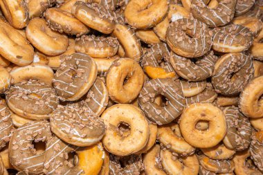 Tatlı ve lezzetli yuvarlak çörekler, şekerle kaplı halka çörekler. Çikolatalı donutlu donut. Şekerin sembolü, kızarmış hamur. Bir sürü tatlı, sağlıksız yemek. Gıda atıkları, gıda üretimi.