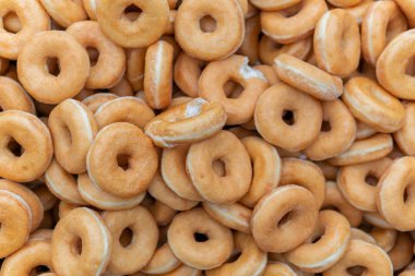 Tatlı ve lezzetli yuvarlak çörekler, şekerle kaplı halka çörekler. Çikolatalı donutlu donut. Şekerin sembolü, kızarmış hamur. Bir sürü tatlı, sağlıksız yemek. Gıda atıkları, gıda üretimi.