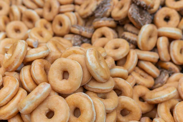 Tatlı ve lezzetli yuvarlak çörekler, şekerle kaplı halka çörekler. Çikolatalı donutlu donut. Şekerin sembolü, kızarmış hamur. Bir sürü tatlı, sağlıksız yemek. Gıda atıkları, gıda üretimi.