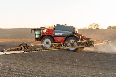 İsveç, Knislinge 10 Mayıs 2023: Traktör gün batımında tarlaya gübre püskürtüyor