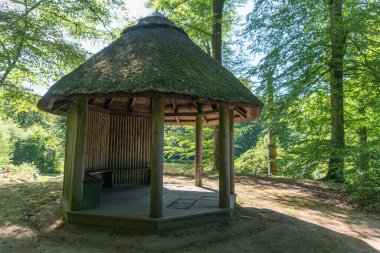 A small gazebo in the forest with a bench for resting clipart