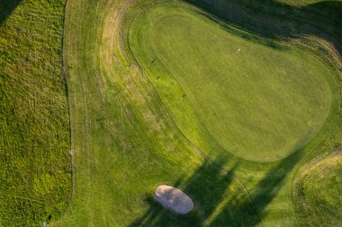 Yazın gün batımında golf sahası, İHA atışı. Güzel gölgeler ve yeşil manikürlü tarla.