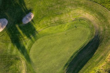 Yazın gün batımında golf sahası, İHA atışı. Güzel gölgeler ve yeşil manikürlü tarla.