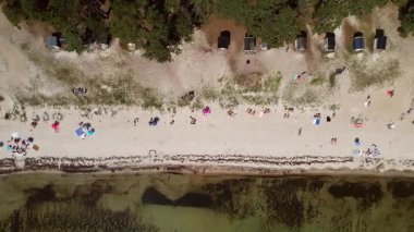 Güneşli bir günde, insanların güneşlendiği ve deniz kenarında dinlendiği güzel bir kumsalın üzerinde insansız hava aracı.