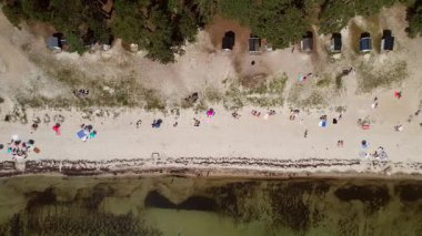 Güneşli bir günde, insanların güneşlendiği ve deniz kenarında dinlendiği güzel bir kumsalın üzerinde insansız hava aracı.
