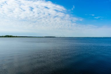 Su yüzeyinde dalgalanmalar ve mavi gökyüzünde bulutlar.