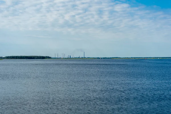 Stock image water surface, ripples on the water and clouds in the blue sky. industrial pipes with smoke on the other side of the tank