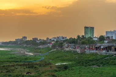 Alacakaranlıkta şehir manzarası turuncu gökyüzüne karşı binalar, kentsel büyüme ve çevresel kontrastı yansıtıyor, Rajshahi Bangladeş seti