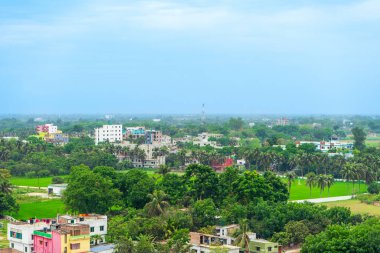 Dağınık binaları ve mavi gökyüzünün altında parlak bulutlu palmiye ağaçları olan yeşil manzara, Radshahi Bangladeş
