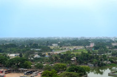 Dağınık binalar ve puslu gökyüzü altındaki ağaçlarla dolu yemyeşil bir arazinin havadan görünüşü. Bangladeş, Rajshahi