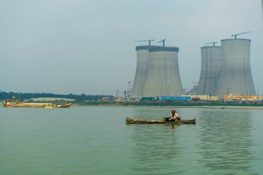 Bangladesh, Ruppur - 29.03.2024: Fisherman in boat on Ganges River, Padma with cooling towers of Rooppur Nuclear Power Plant under construction in background clipart