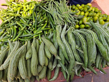 Bir markette sergilenen çeşitli taze yeşil sebzeler. Bamya, trichosanthes, abelmoschus esculentus, uzun fasulyeler, kabak ve limon, hepsi düzgün sıralanmış.