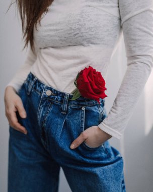 Beyaz uzun bacaklı zayıf bir kadın ve kotunun cebinde kırmızı bir gül ve eli olan bir kot pantolon.