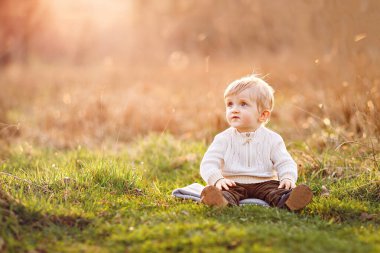 Güzel, güneşli arka planda çimlerin üzerinde oturan tatlı sarışın çocuk.