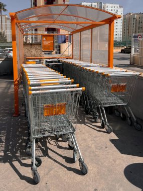 Valencia, İspanya - 1 Nisan 2025: Metal süpermarket alışveriş arabaları şeffaf çatı altında, açık hava sığınak alanında düzenli olarak düzenlenmiştir.