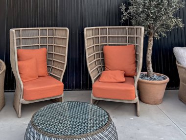 Bir çift modern açık hava şezlongları parlak turuncu minderleri ve karanlık duvarda kahve masası, şık veranda oturma konsepti.