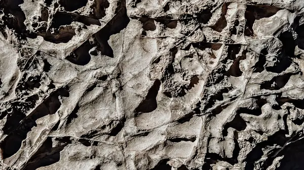Kabataslak yüzeyli soyut doğal kaya dokusu, desenler, çatlaklar ve gölgeler, detaylı toprak oluşumu, organik doğal fon materyali, yakın plan görünümü