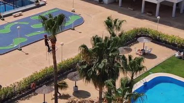 Valencia, İspanya - 17 Haziran 2025: İşçi, konut kompleksinde yüzme havuzu yakınında tırmanma ekipmanlarıyla uzun palmiye ağaçlarını buduyor