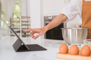 Mutfakta fırın yapan kadın tablet izliyor..