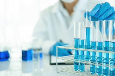 Tıbbi ya da bilimsel araştırmacı ya da insan doktoru laboratuarda bir test tüpü dolusu temiz çözeltiye bakıyor.