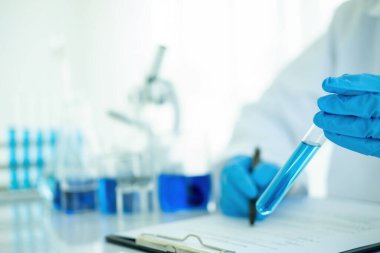 Tıbbi ya da bilimsel araştırmacı ya da insan doktoru laboratuarda bir test tüpü dolusu temiz çözeltiye bakıyor.