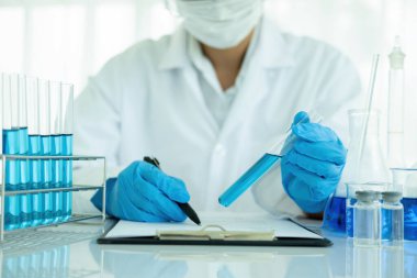 Tıbbi ya da bilimsel araştırmacı ya da insan doktoru laboratuarda bir test tüpü dolusu temiz çözeltiye bakıyor.