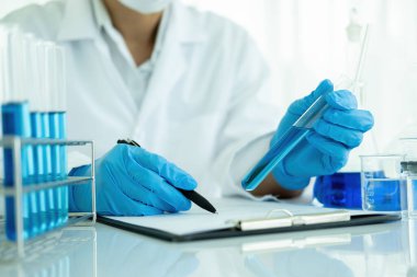 Tıbbi ya da bilimsel araştırmacı ya da insan doktoru laboratuarda bir test tüpü dolusu temiz çözeltiye bakıyor.
