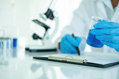 Tıbbi ya da bilimsel araştırmacı ya da insan doktoru laboratuarda bir test tüpü dolusu temiz çözeltiye bakıyor.