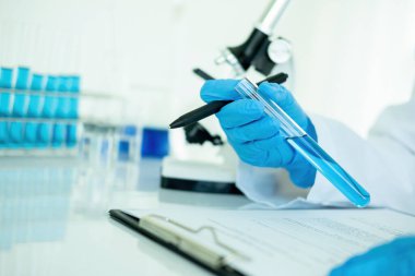 Tıbbi ya da bilimsel araştırmacı ya da insan doktoru laboratuarda bir test tüpü dolusu temiz çözeltiye bakıyor.