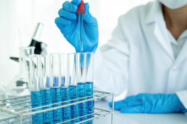 Tıbbi ya da bilimsel araştırmacı ya da insan doktoru laboratuarda bir test tüpü dolusu temiz çözeltiye bakıyor.