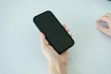 Modern bir odada oturan bir kadının kapalı çekilmiş bir fotoğrafı. Akıllı telefonunu arayarak, mesajlaşarak, internette gezinerek, bilgi arayarak ya da arkadaşlarıyla mesajlaşarak....