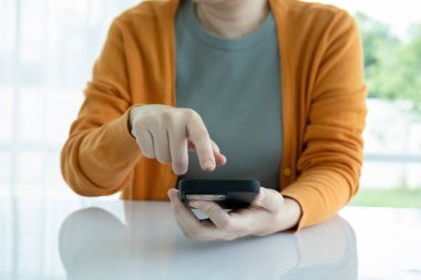 Modern bir odada oturan bir kadının kapalı çekilmiş bir fotoğrafı. Akıllı telefonunu arayarak, mesajlaşarak, internette gezinerek, bilgi arayarak ya da arkadaşlarıyla mesajlaşarak....