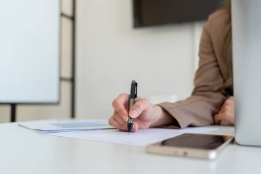 İş kadını iş yerindeki koltukta ya da evdeki koltukta oturuyor ve şirket için iş planı ve stratejiler oluşturmak için dizüstü bilgisayar üzerinde çalışıyor, grafikler ve kağıtlar üzerindeki verileri analiz ediyor ve kağıtlara yazıyor..