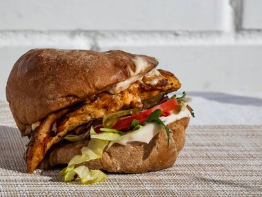 Izgara tavuk filetosu, ciabata, burger sosu, roka, pesto, balzamik, salata, turşu, domates, kırmızı soğan ile sulu tavuk burgerini yakından çek.