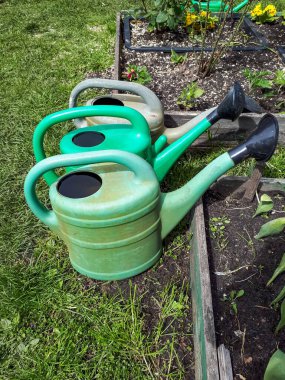 Bahçedeki parlak güneş ışığında bitkileri sulamak için yerdeki yeşil plastik sulama kutuları. Bahçe manzarası
