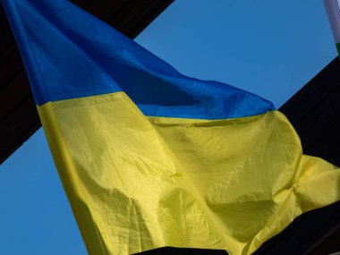 Mavi ve sarı Ukrayna bayrağı gökyüzünde, bina duvarının yanındaki bayrak direğinde parlak güneş ışığında dalgalanıyor. Ukrayna 'nın ulusal bayrağında iki eşit büyüklükte mavi ve sarı yatay şerit vardır.