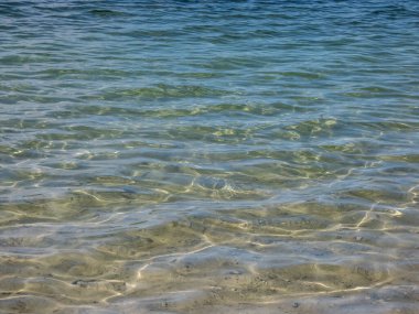 Mavi, yeşil ve turkuazın tonlarında kristal şeffaf su. Suyun hareketindeki güneşin parlak yansımasıyla bembeyaz kum tabanı.