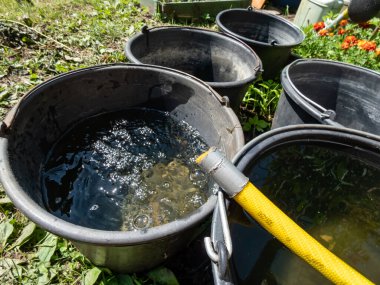 Yaz sıcağında bahçede plastik bir hortumdan boşalan suyla dolu boş plastik kovaların manzarası