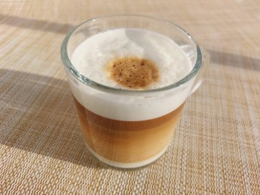 Kapuçino bardakta sıcak kapuçino, köpüklü süt köpüğü ve kahve kapsüllerinden yapılan espresso ile yakın plan bir çekim.