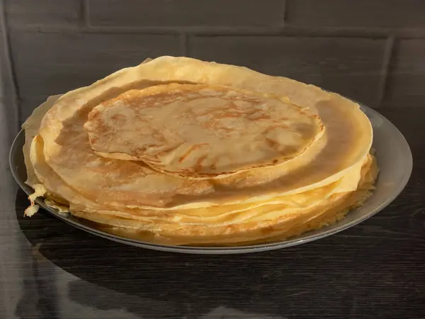 Gri bir masanın üzerinde ince, altın renkli güneş ışığı krepleri olan bir tabağın yakın çekimi. Gıda manzarası