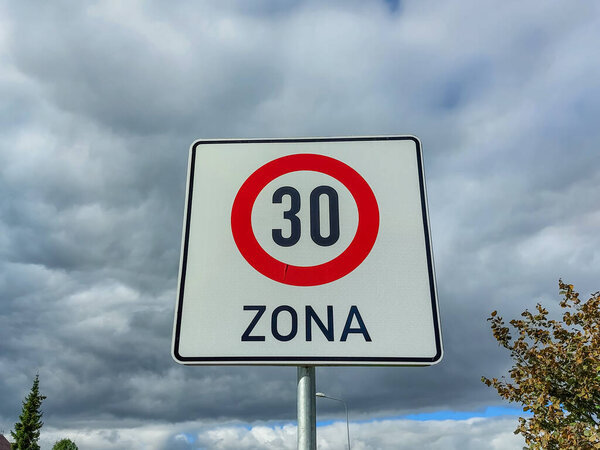 Metal road or traffic sign with number 30 in a red circle, and zone, indicating new speed limit against blue sky and clouds background