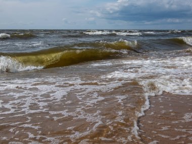 Baltık Denizi 'nin güzel deniz manzarası rüzgarlı bir günde büyük köpüklü dalgalar kıyıda kahverengi kumlar ve yukarıda mavi gökyüzü