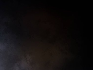 Takım elbiseli ve kravatlı bir adam karanlık bir arka planın önünde duruyor.