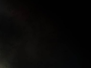 Takım elbiseli ve kravatlı bir adam karanlık bir arka planın önünde duruyor.