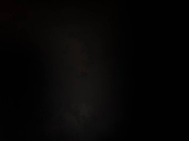 Siyah gömlekli bir adam karanlıkta dikiliyor.