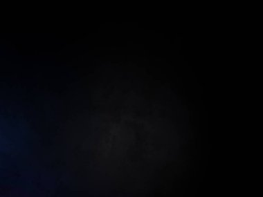 Siyah bir arka planın önünde duran takım elbiseli ve kravatlı bir adam.