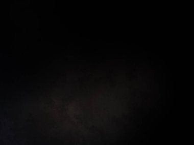 Takım elbiseli ve kravatlı bir adam karanlık bir arka planın önünde duruyor.