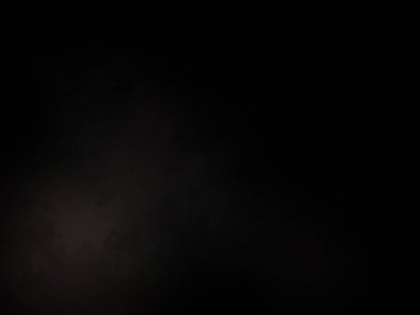 Siyah bir arka planın önünde duran takım elbiseli ve kravatlı bir adam.