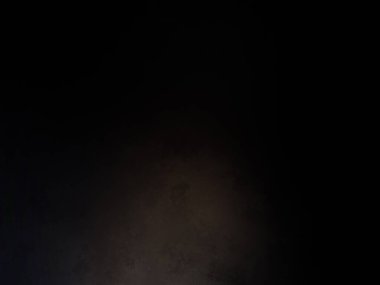 Siyah duvarın önünde duran takım elbiseli ve kravatlı bir adam.