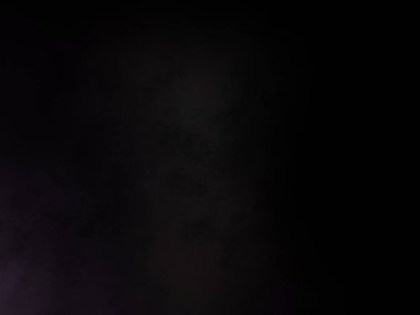 Takım elbiseli ve kravatlı bir adam karanlık bir arka planın önünde duruyor.